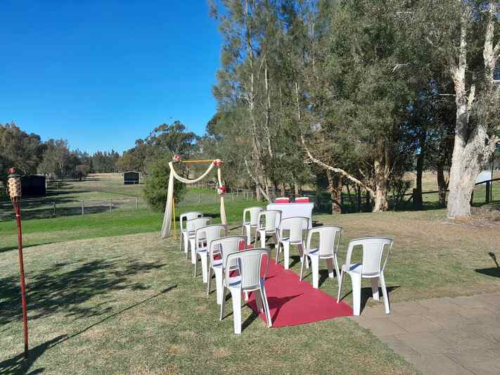 Outdoor wedding ceremony setup with chairs, red carpet, and a simple arch under a clear blue sky
